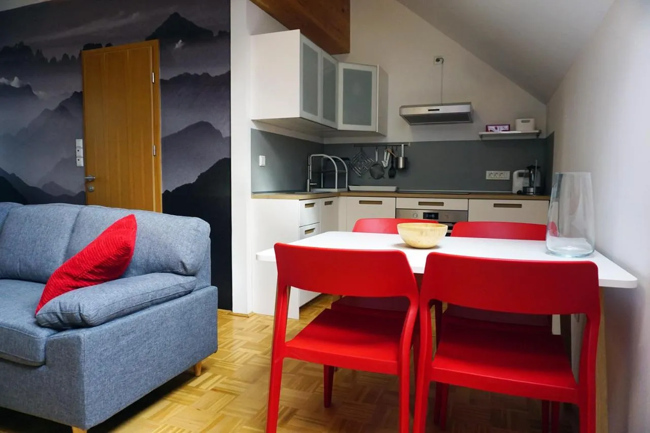Jedilna miza z rdečimi stoli in kuhinja v apartmaju Rdeče obzorje